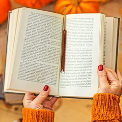 Person in orange sleeves holding an open book with a brown bookmark between the pages.