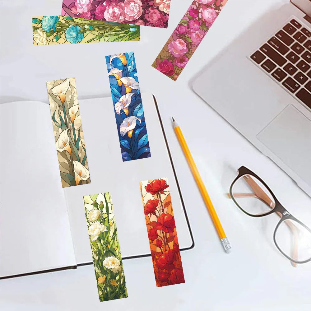 Floral paper bookmarks beside a laptop, notebook, and glasses.
