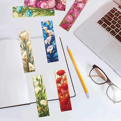 Floral paper bookmarks beside a laptop, notebook, and glasses.