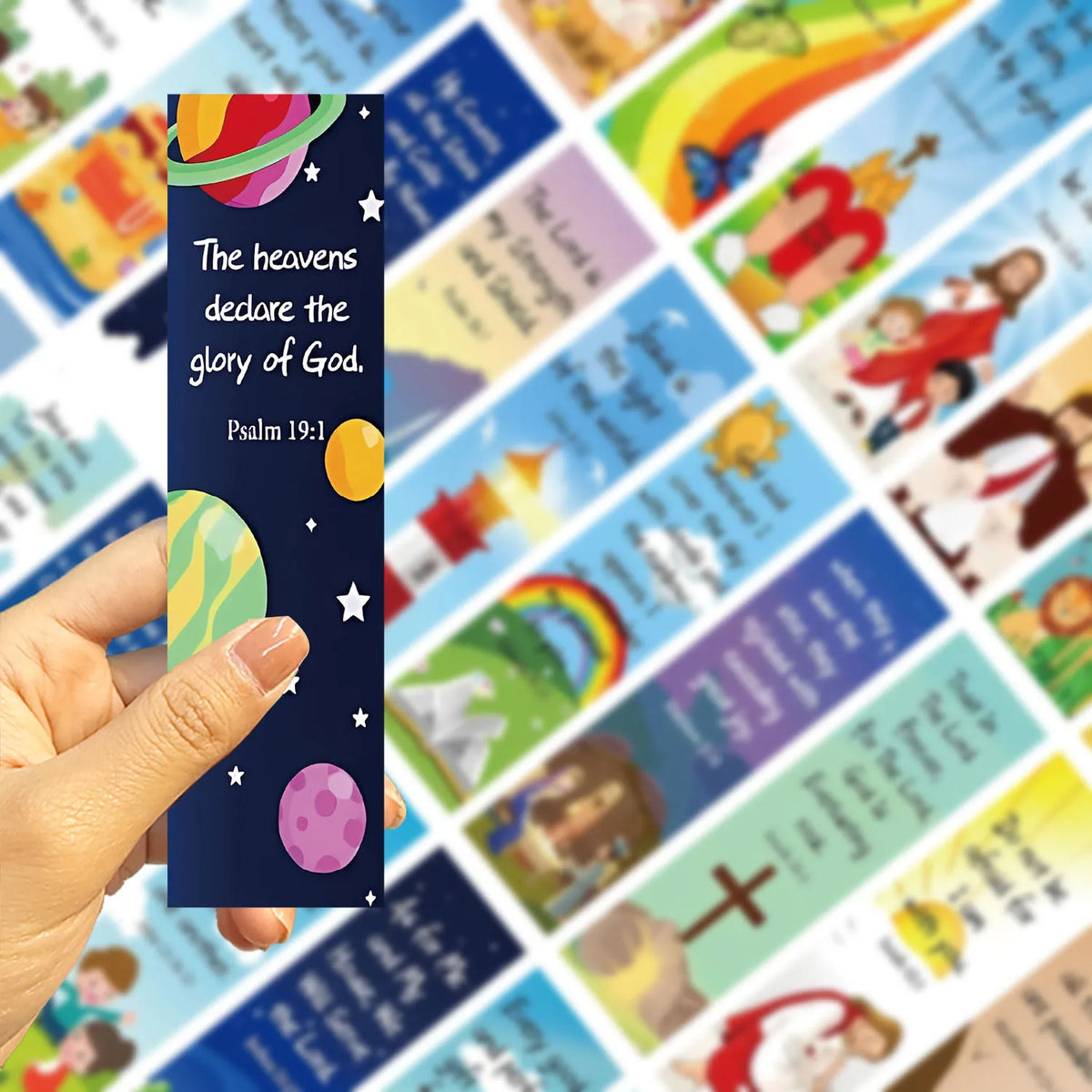Hand holding a planets-and-stars bookmark with Psalm 19:1 wording
