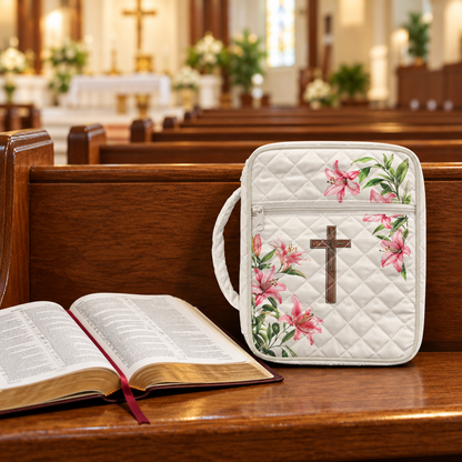 White quilted case with pink lilies and a cross on a church pew beside an open Bible.
